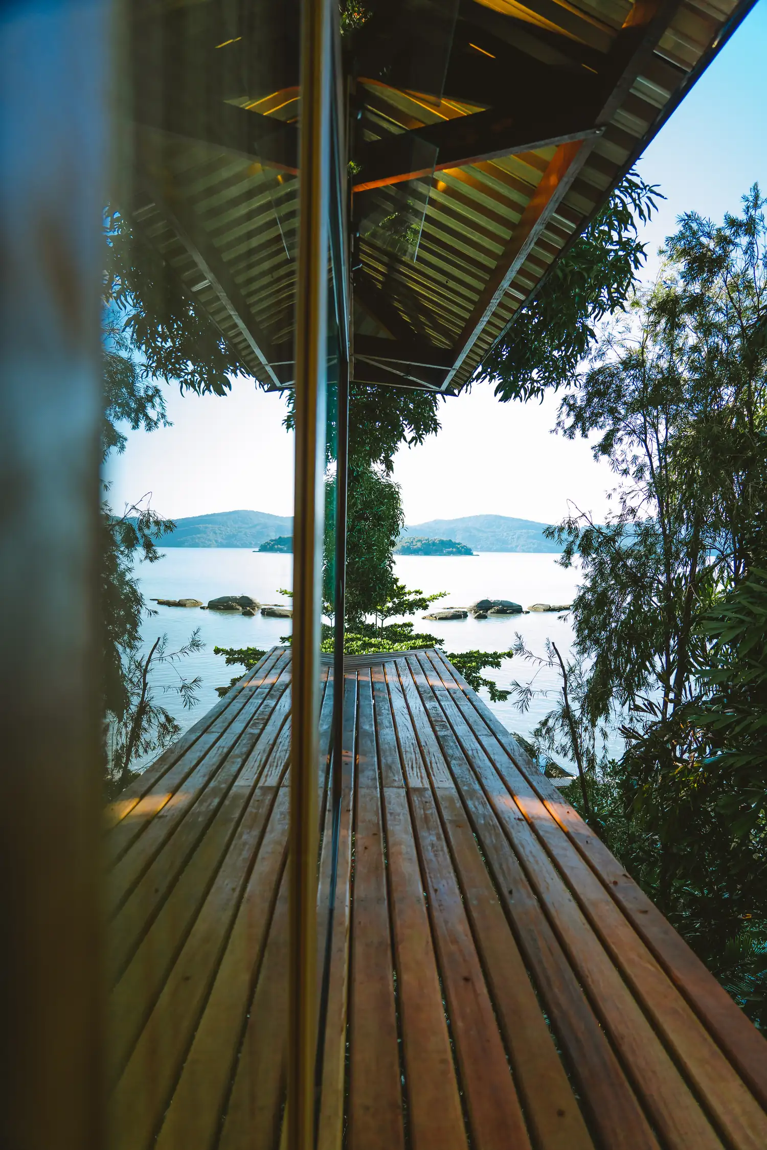 Manhã clara vista da proa da Casa Proa, com o deque de madeira apontando para as ilhas da Baía de Paraty