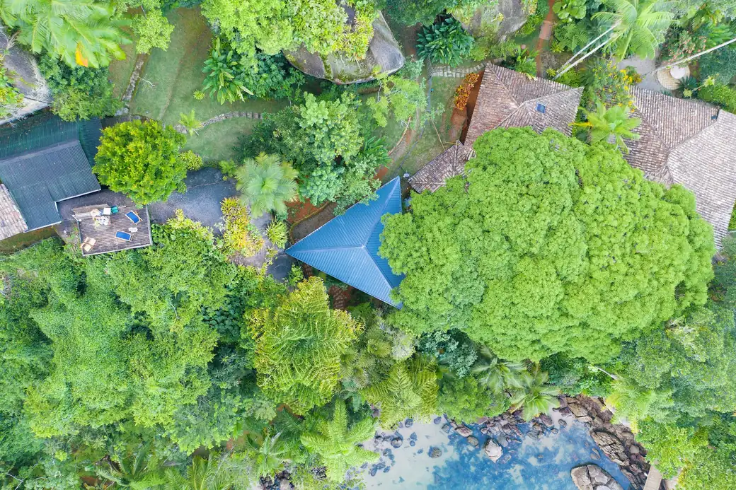 O telhado em tetraedro da Casa Proa, um triângulo azul visto de cima, cercado pela mata